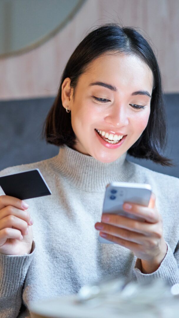 portrait smiling korean woman using credit card smartphone app paying purchase order onli